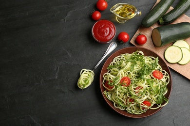Photo of Delicious zucchini pasta with arugula and cherry tomatoes served on black slate table, flat lay. Space for text