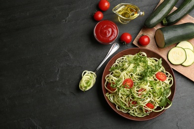 Delicious zucchini pasta with arugula and cherry tomatoes served on black slate table, flat lay. Space for text