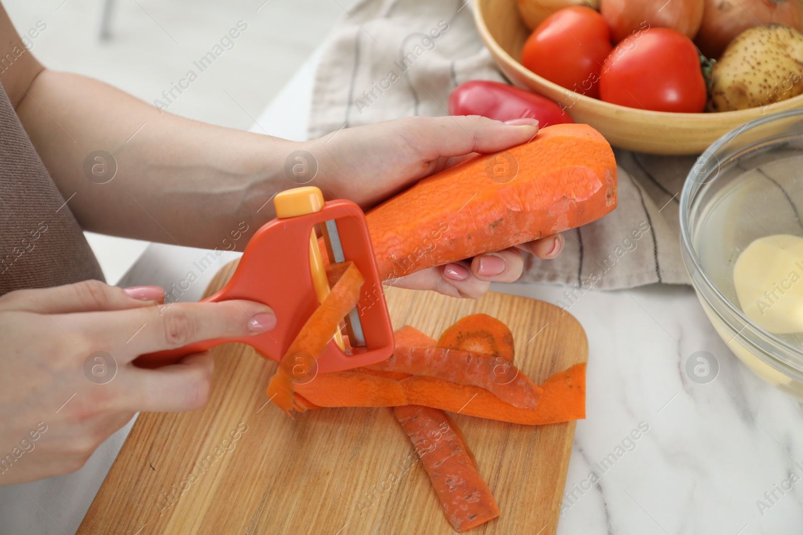 Photo of Woman peeling fresh carrot at white marble table, closeup