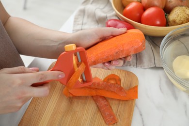 Photo of Woman peeling fresh carrot at white marble table, closeup