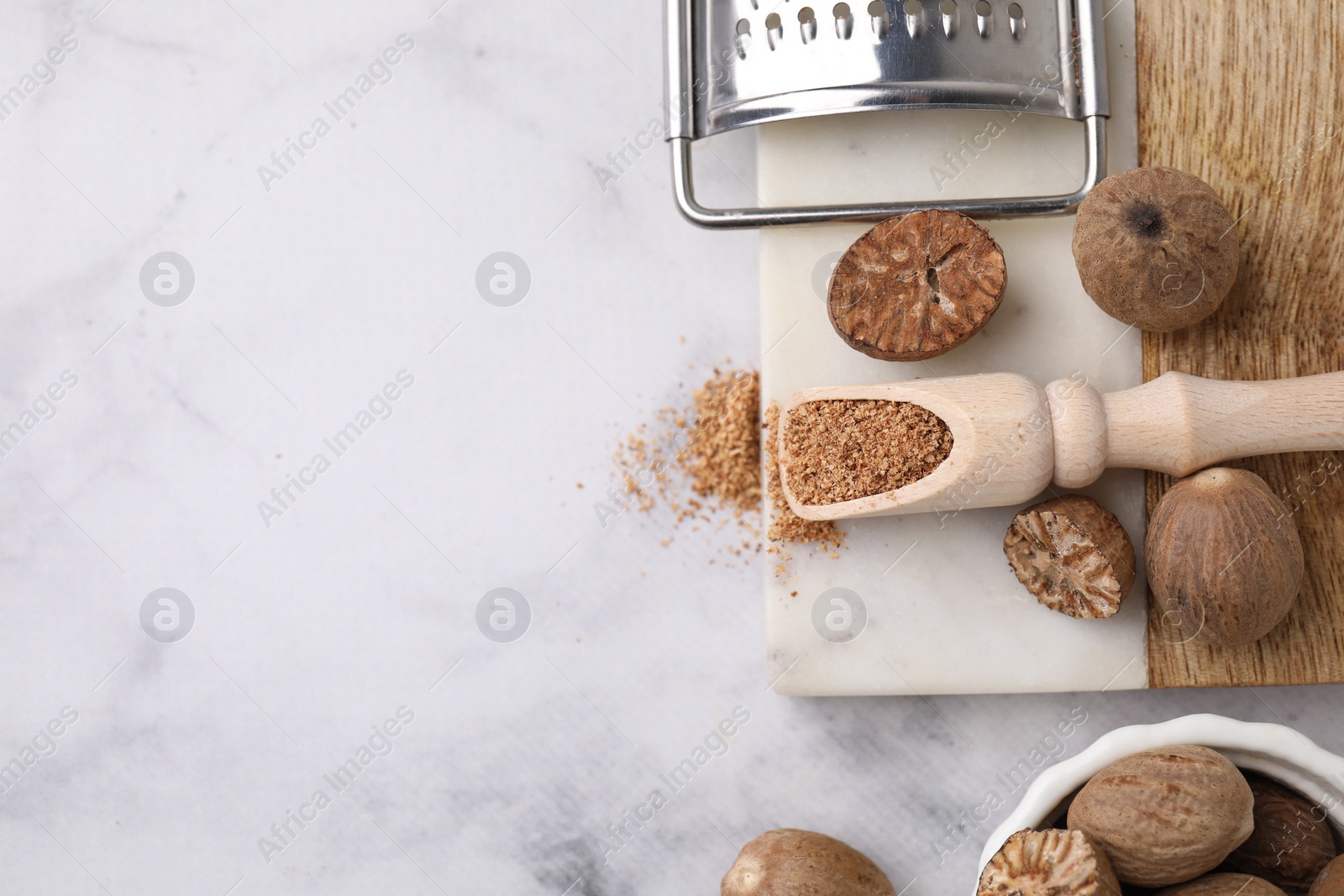 Photo of Scoop with grated nutmeg, seeds and grater on white marble table, flat lay. Space for text