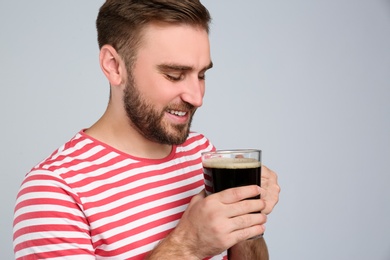 Photo of Handsome man with cold kvass on light grey background. Traditional Russian summer drink