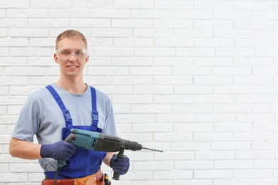Photo of Handsome young working man with rotary hammer indoors, space for text. Home repair