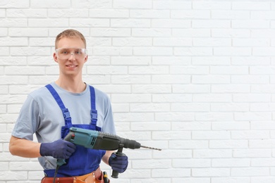 Handsome young working man with rotary hammer indoors, space for text. Home repair