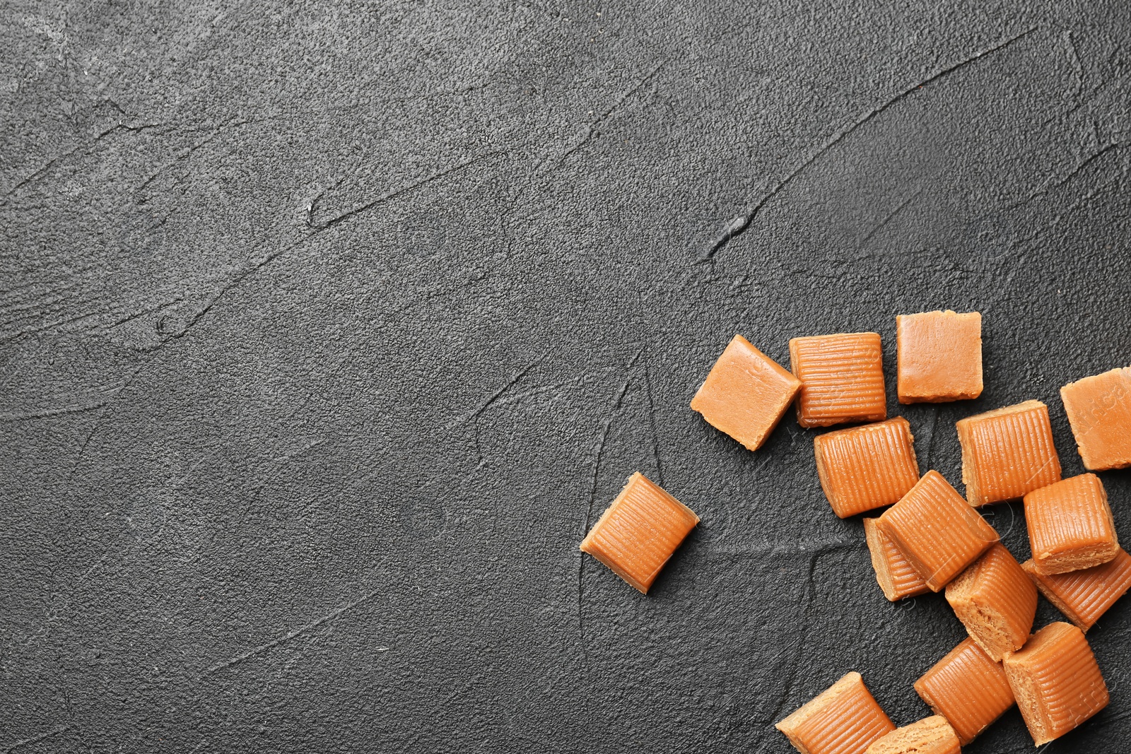 Photo of Delicious caramel candies on dark background, top view