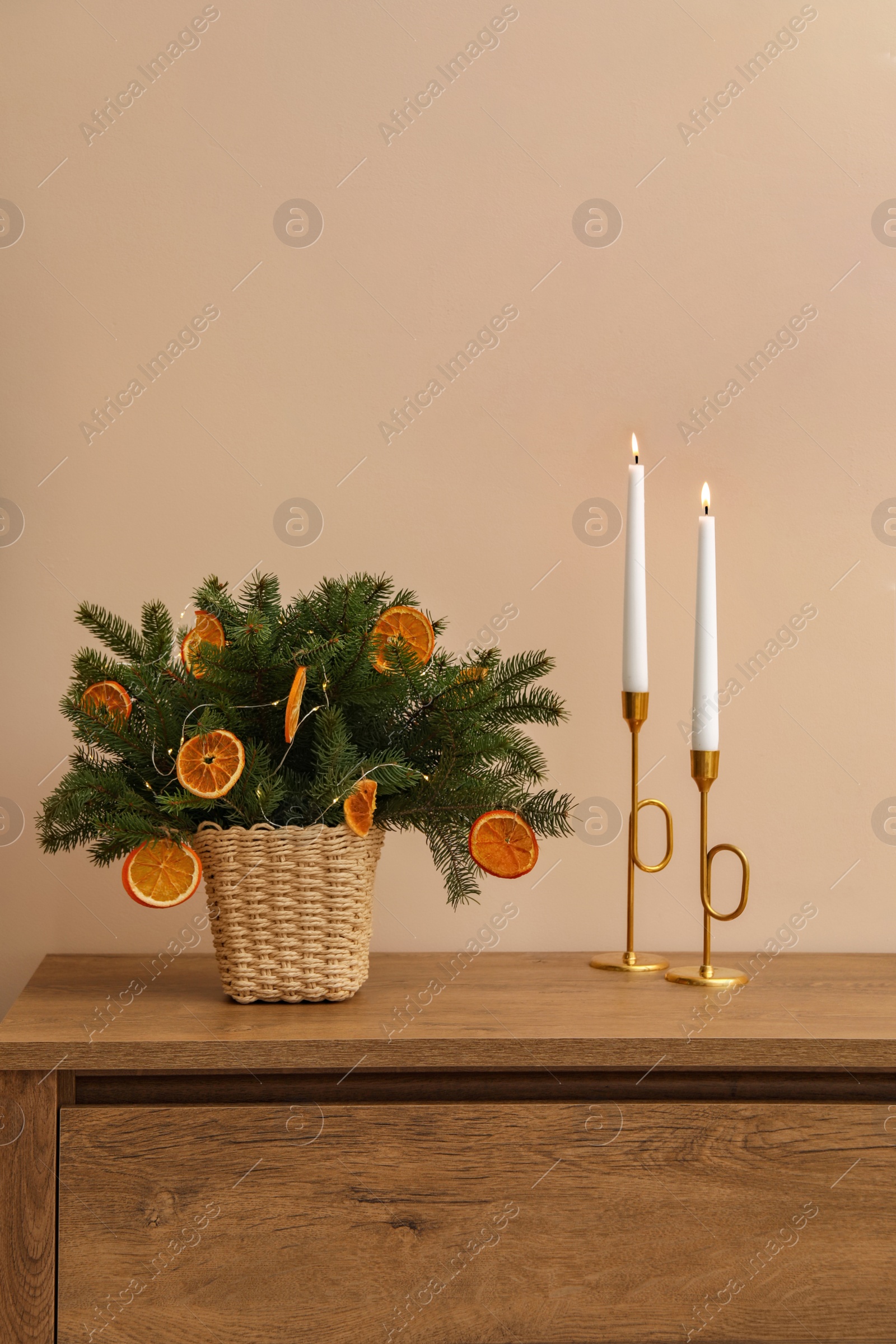 Photo of Wicker basket with fir tree branches and dried orange slices on wooden table near beige wall. Decor for stylish interior