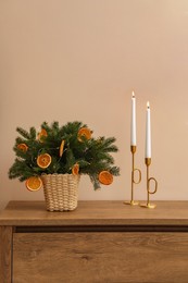 Wicker basket with fir tree branches and dried orange slices on wooden table near beige wall. Decor for stylish interior