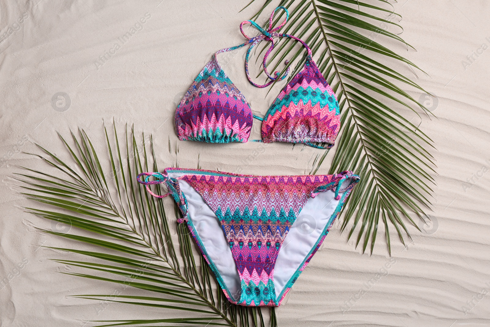 Photo of Stylish swimsuit and leaves on sand, flat lay. Beach accessory