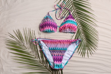 Photo of Stylish swimsuit and leaves on sand, flat lay. Beach accessory