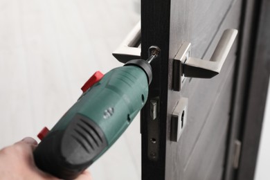 Handyman with electric screwdriver repairing door handle indoors, closeup