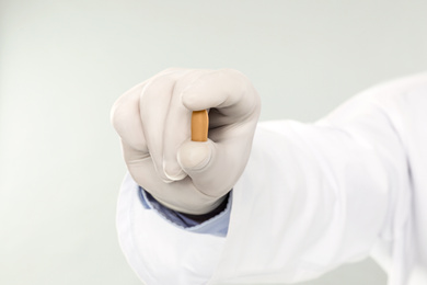 Photo of Doctor holding suppository for hemorrhoid treatment on light grey background, closeup