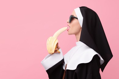Photo of Woman in nun habit with banana against pink background, space for text. Sexy costume