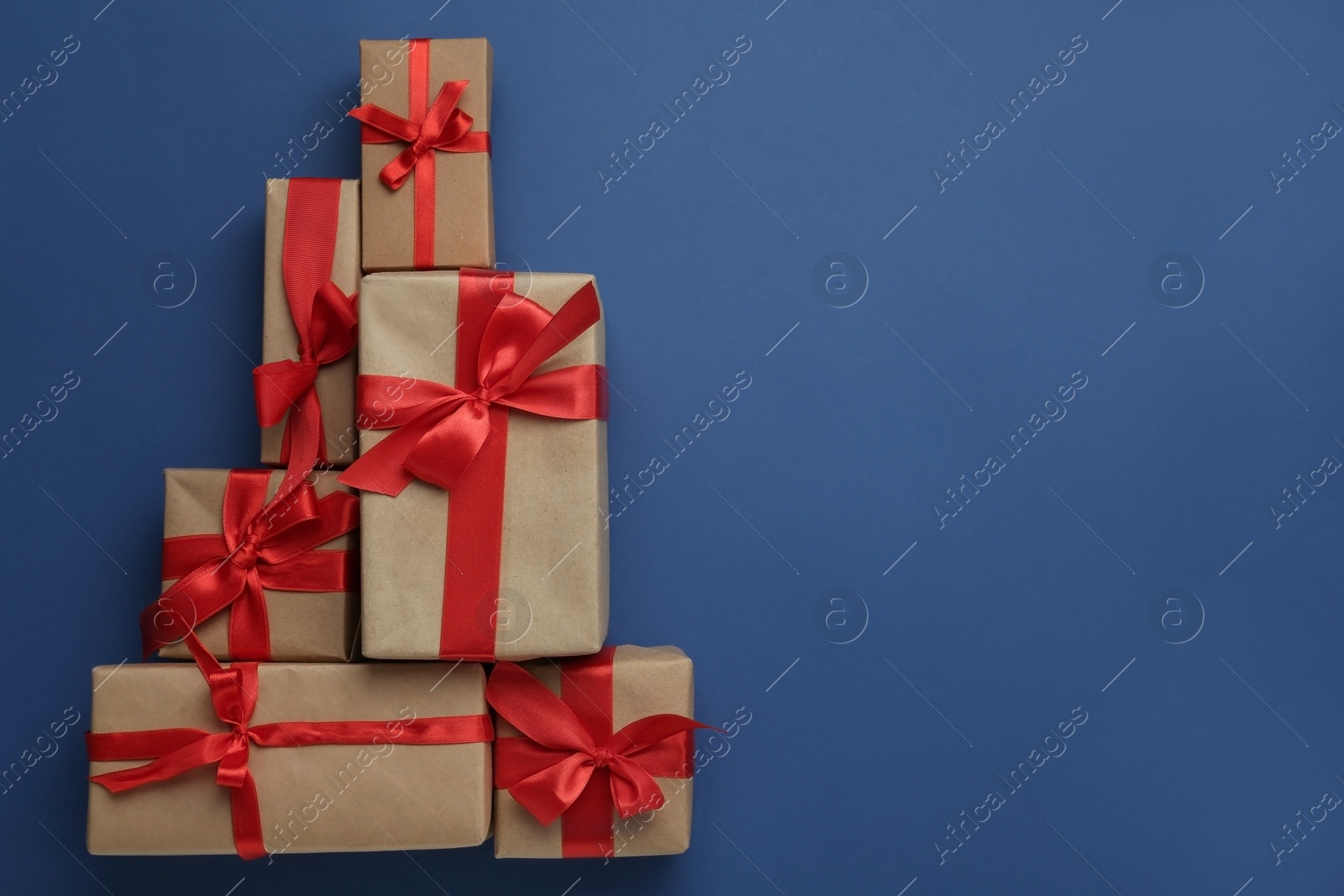 Photo of Christmas tree shape of gift boxes on blue background, flat lay. Space for text