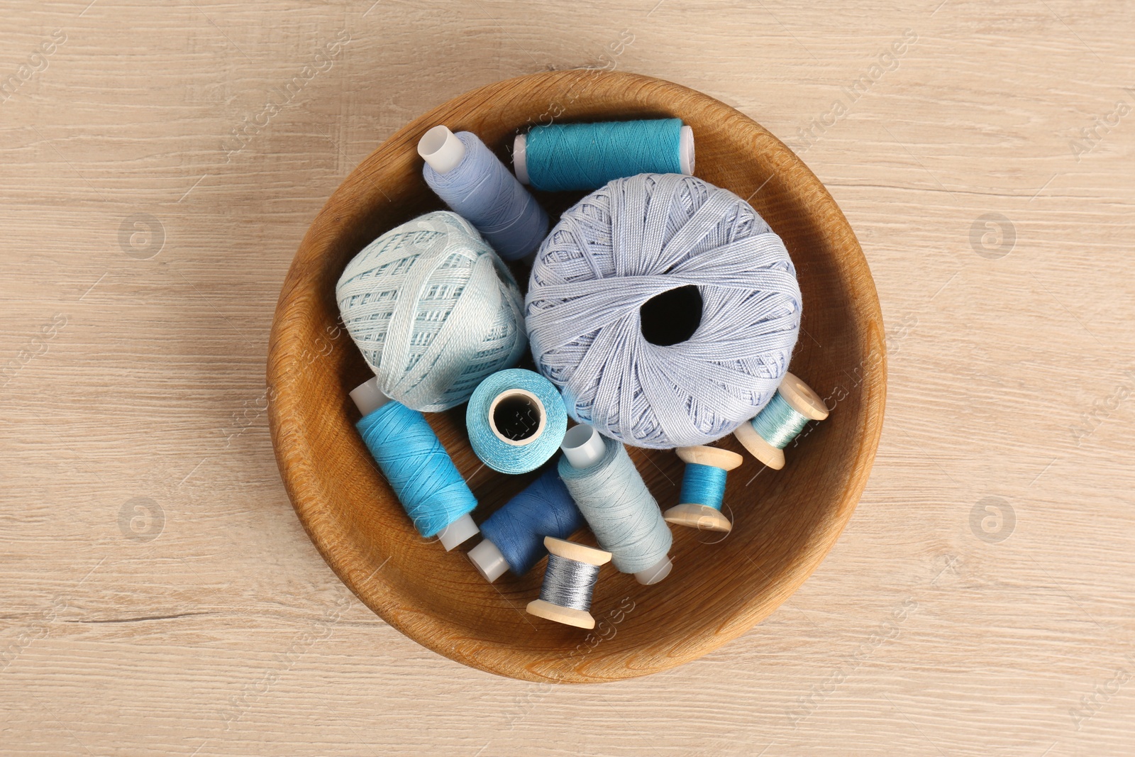 Photo of Color sewing threads in bowl on wooden table, top view