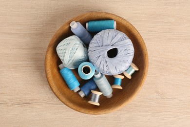 Photo of Color sewing threads in bowl on wooden table, top view