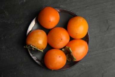 Photo of Tasty ripe persimmons on black slate table, top view