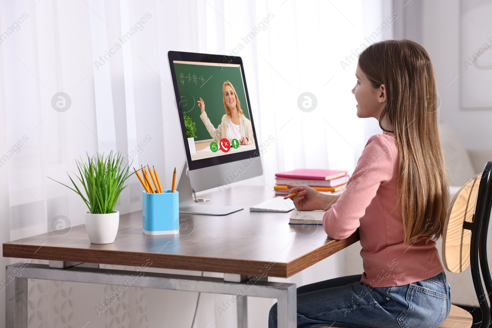 Image of E-learning. Little girl taking notes during online lesson at wooden table