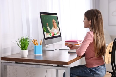 Image of E-learning. Little girl taking notes during online lesson at wooden table
