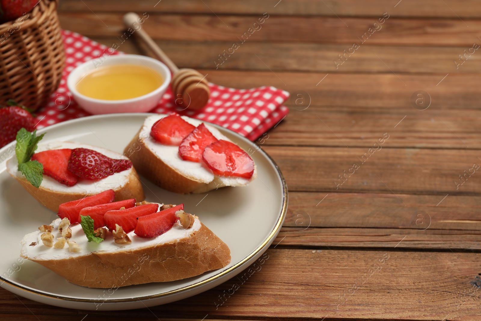 Photo of Delicious bruschettas with ricotta cheese, walnuts, mint, strawberries and honey on wooden table, closeup. Space for text