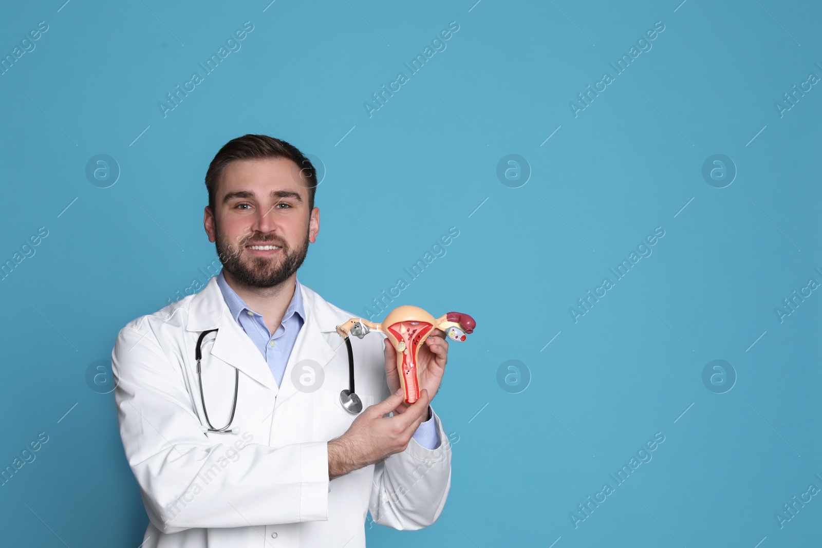 Photo of Doctor demonstrating model of female reproductive system on light blue background, space for text. Gynecological care