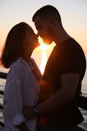 Photo of Happy young couple kissing on sea embankment at sunset