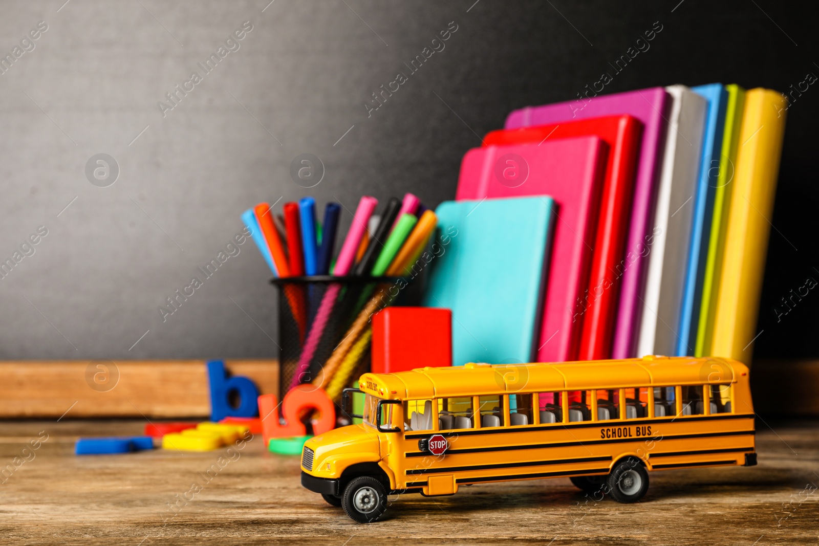 Photo of School bus model and stationery on wooden table. Transport for students