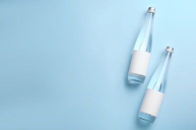 Photo of Glass bottles of water with blank labels on light blue background, flat lay. Space for text