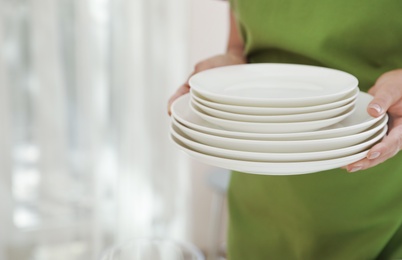 Photo of Woman holding stack of clean dishes indoors, closeup. Space for text