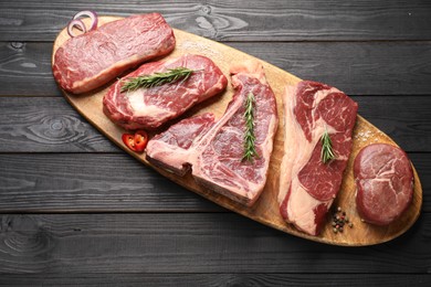 Photo of Pieces of raw beef meat and spices on black wooden table, top view