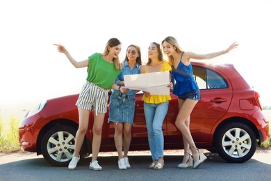 Photo of Happy beautiful young women with map standing near car in countryside