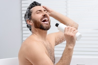 Photo of Happy man with bottle of shampoo singing in shower