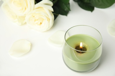 Photo of Burning candle in glass holder and roses on white table, space for text