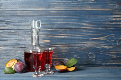 Photo of Delicious plum liquor and ripe fruits on blue wooden table. Homemade strong alcoholic beverage