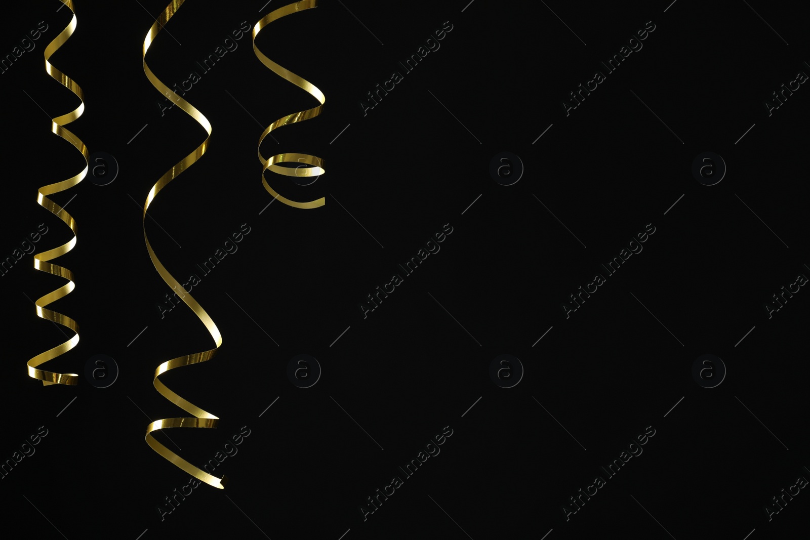 Photo of Shiny golden serpentine streamers on black background. Space for text