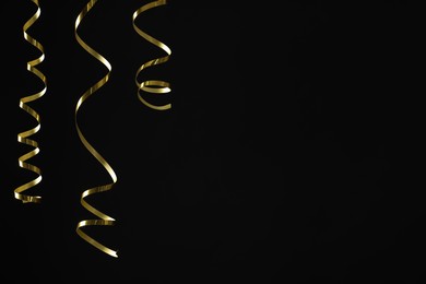 Photo of Shiny golden serpentine streamers on black background. Space for text