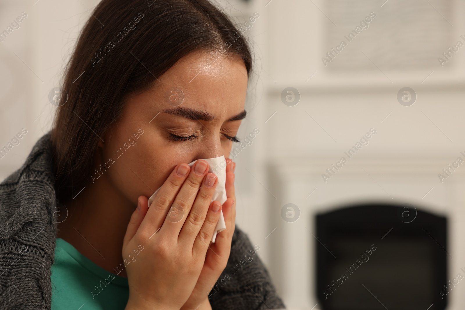 Photo of Sick woman wrapped in blanket with tissue blowing nose at home, closeup and space for text. Cold symptoms