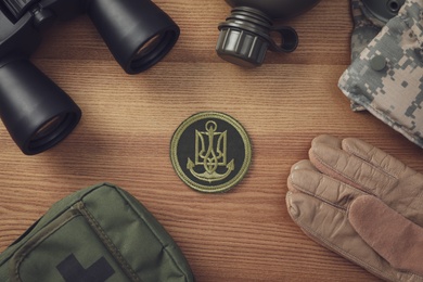 Photo of MYKOLAIV, UKRAINE - SEPTEMBER 26, 2020: Tactical gear and Ukrainian army patch on wooden table, flat lay