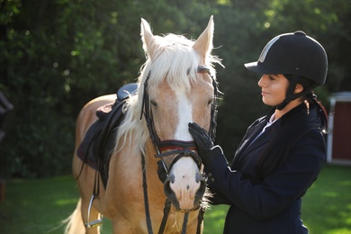 Photo of Young woman in horse riding suit and her beautiful pet outdoors on sunny day