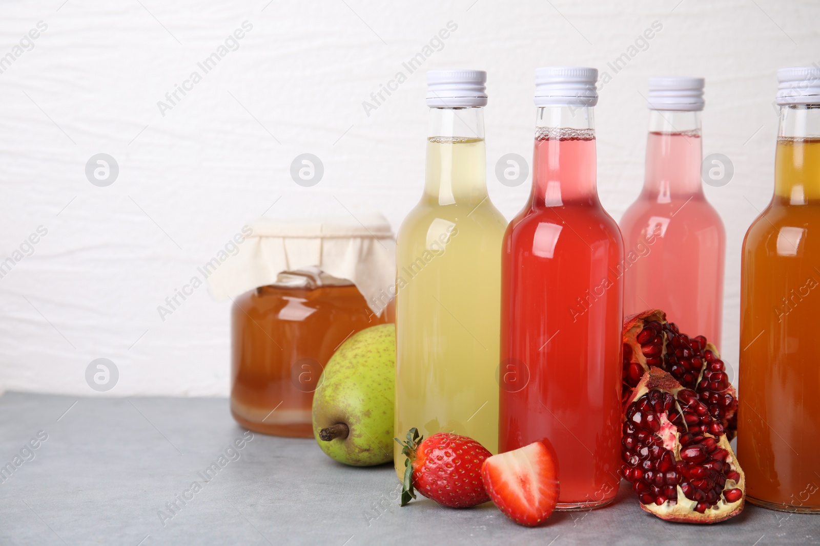 Photo of Delicious kombucha in glass bottles, jar and fresh fruits on grey table against white background, space for text