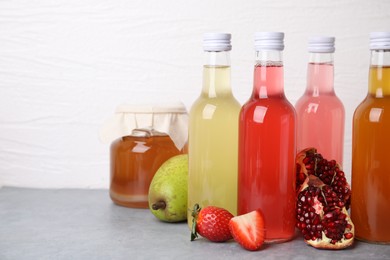 Delicious kombucha in glass bottles, jar and fresh fruits on grey table against white background, space for text