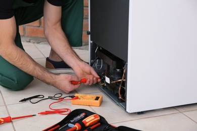 Photo of Male technician repairing broken refrigerator indoors, closeup