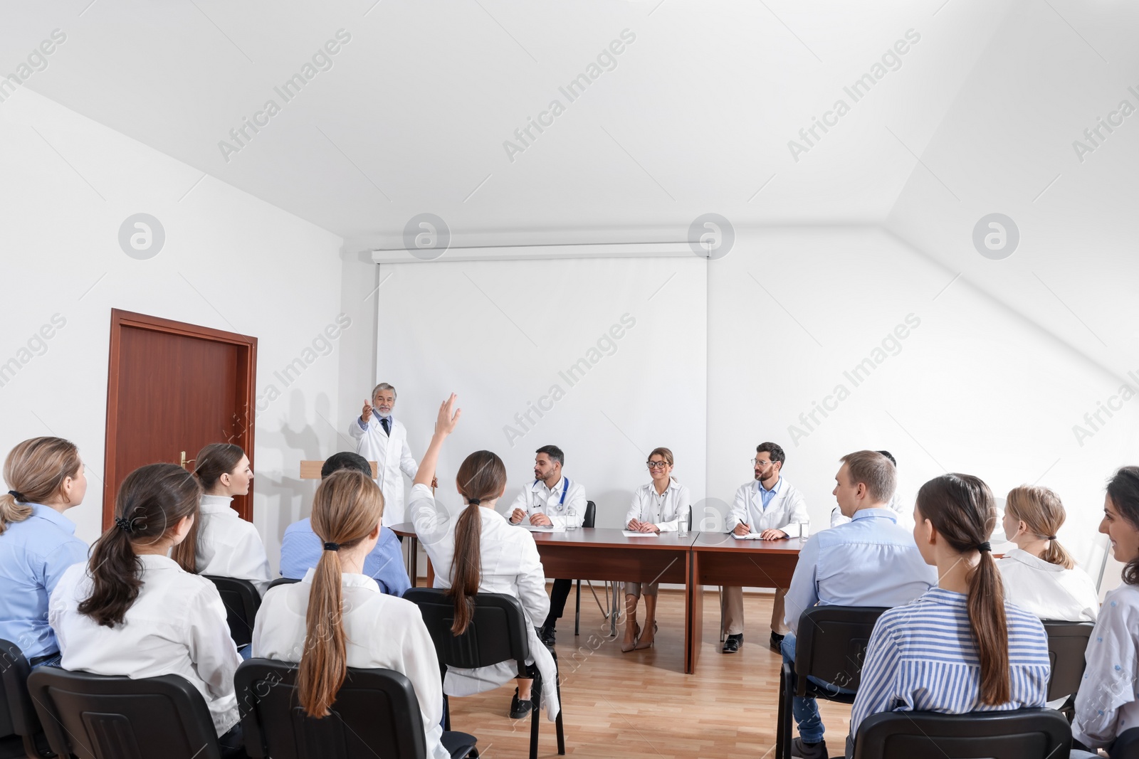 Photo of Senior doctor giving lecture in conference room with projection screen