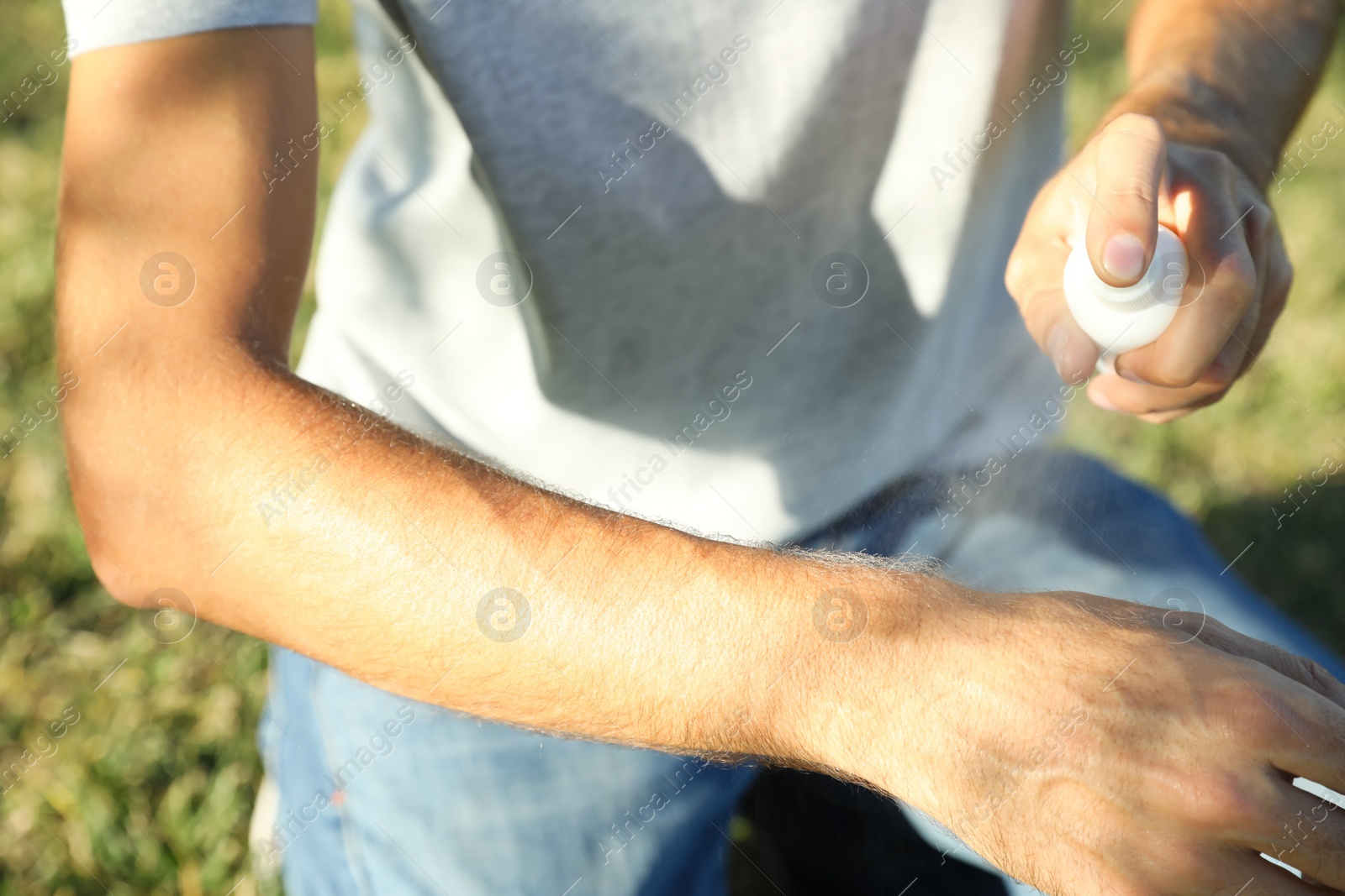 Photo of Man applying insect repellent onto arm outdoors, closeup