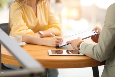 Woman signing contract with insurance agent in office, closeup