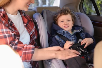 Photo of Mother fastening her son in child safety seat inside car