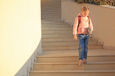 Photo of Cute little girl with backpack and textbooks on stairs outdoors. Space for text