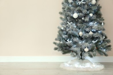 Photo of Decorated Christmas tree with white faux fur skirt near beige wall. Space for text