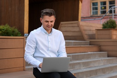Handsome man using laptop on bench outdoors. Space for text
