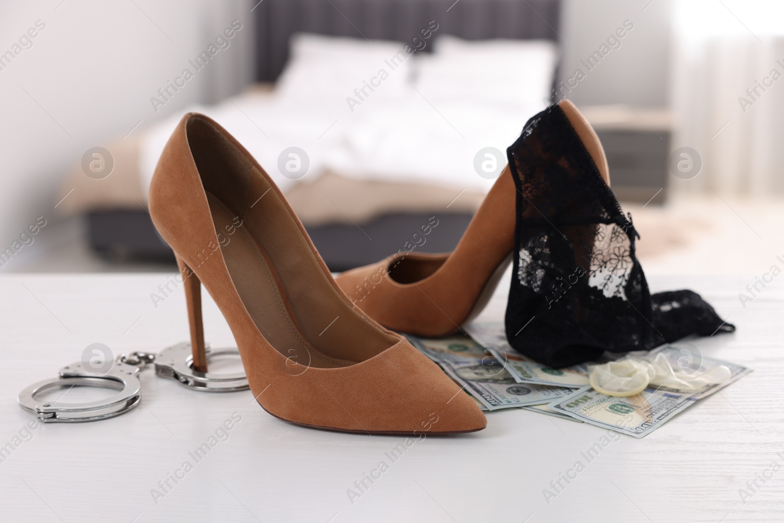 Photo of Prostitution concept. High heeled shoes, handcuffs, panties, dollar banknotes and condom on white wooden table indoors, closeup