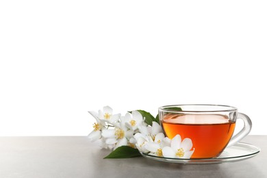 Photo of Glass cup of aromatic jasmine tea and fresh flowers on grey table against white background. Space for text
